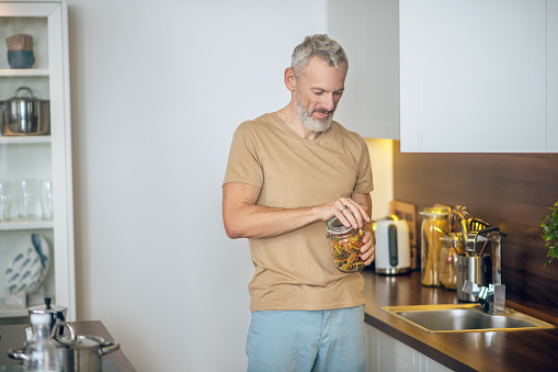 In the kitchen. Mature bearded man in beige tshirt in the kitchen at home