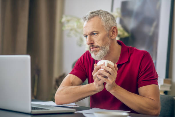 istock Grey-haired man sitting at the laptop and having coffee 1290884358