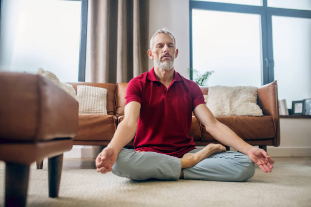istock Grey-haired man sitting on the floor in a lotus pose 1290884372