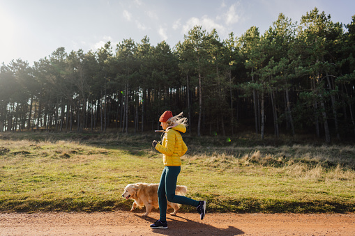 Photo of a young woman jogging with her golden retriever, who keeps her company during exercise