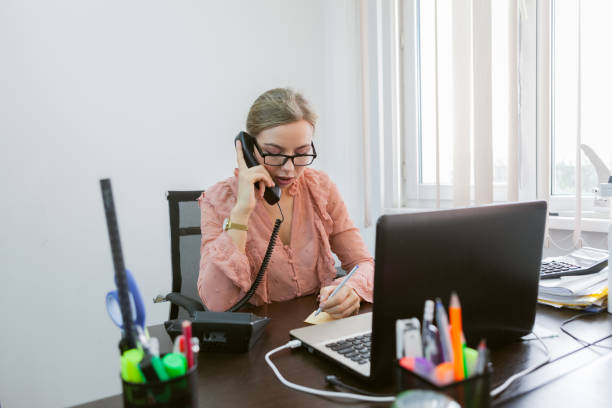 istock Everything is in work. Office worker woman talking on the phone while sitting at the table with a laptop in the office 1290888227