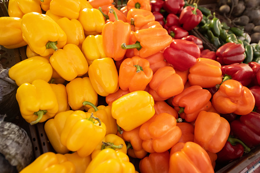 This is a photograph of yellow, orange, and red bell peppers in a pile for sale at an outdoor farmers market in Apopka, Florida.