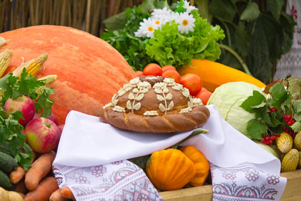 On a white towel is a beautifully decorated cake, nearby there are a variety of vegetables and fruits such as pumpkin, cabbage, apples, carrots.