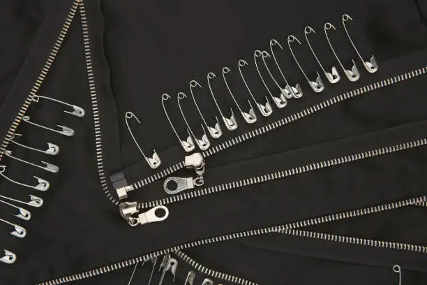 Photo of Safety pins and zippers on black fabric.