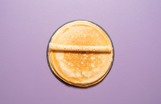 Top view with a stack of fresh homemade pancakes isolated on a purple background. Freshly baked crepes above view.