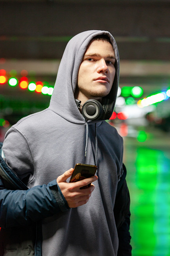 Close up outdoors portrait of 18 year old man in hooded shirt with mobile phone and with headphones