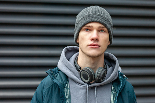 Close-up outdoors portrait of 18 year old man in a hooded shirt in a knit hat and with headphones