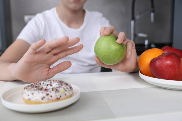 el niño se niega a comer dulces poco saludables y elige frutas para el postre. alimentación saludable y concepto de estilo de vida activo - grasa saturada fotografías e imágenes de stock