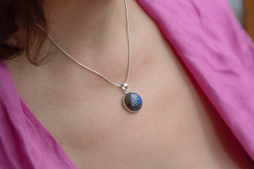 Detail of woman neckline wearing labradorite mineral stone pendant on silver chain