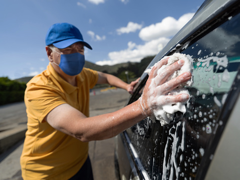 Adult Latin American man working at a car wash wearing a facemask while cleaning the windows â reopening of businesses during the COVID-19 pandemic