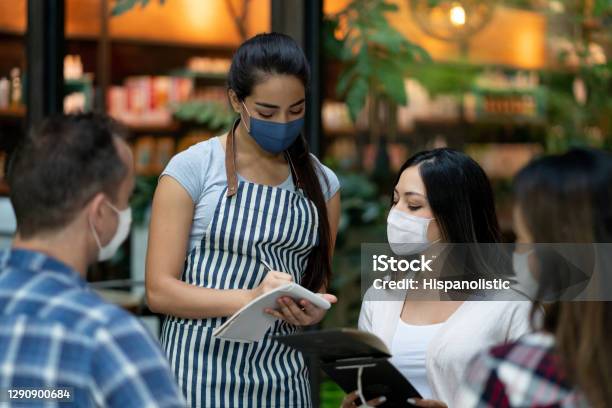 Waitress Working At A Restaurant During The Pandemic And Wearing A Facemask Stock Photo - Download Image Now