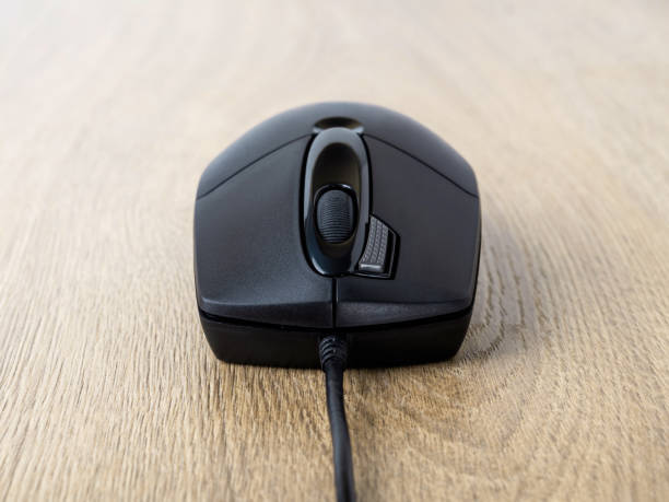istock Close-up of black wired optical mouse over brown desk. Work or study at the computer at home or in the office. 1290901707