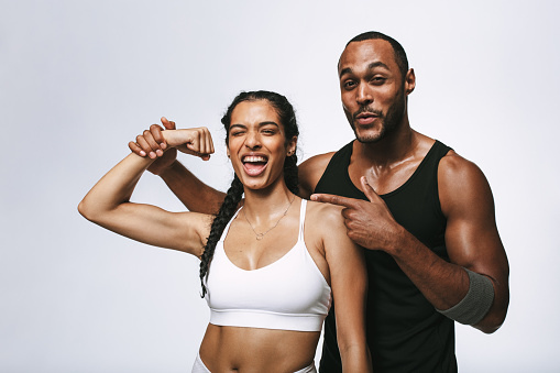 Couple in fitness wear standing together enjoying after workout. Smiling woman showing biceps standing with her male friend.