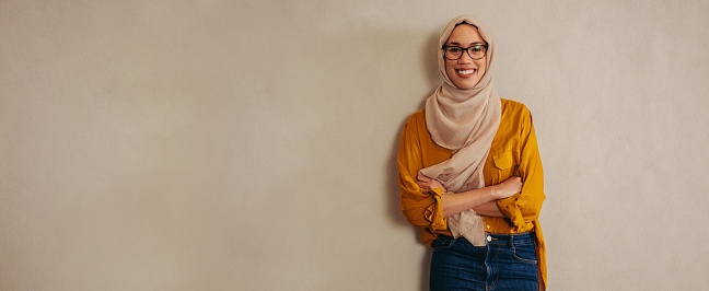 Portrait of a happy muslim woman standing against a wall. Female entrepreneur looking at camera and smiling.