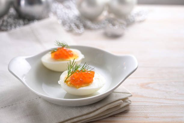 istock Halved eggs with red caviar and dill garnish on a light gray wooden table with Christmas decoration, festive snack for a holiday party, copy space, selected focus 1290904549