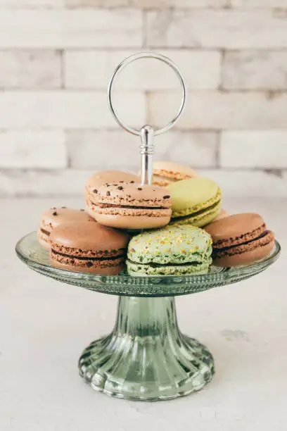 Colourful french macarons on a glass etagere in front of a white wall. Pastries, desserts and sweets. Vertical stock photo.