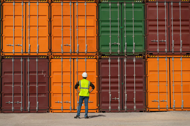 istock Engineer man with white safety helmet and worker west checking cargo freights in front of colorful cargo container stacks in shipping port 1290911088