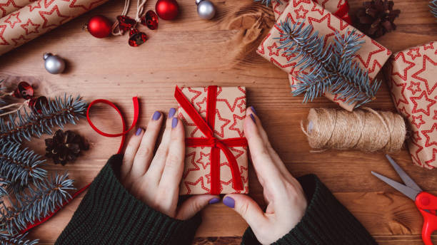 istock Women's hands are wrapping a Christmas gift a wooden background. 1290912575