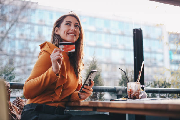 Young woman enjoying in hot chocolate in café, paying he bill with her credit card. COVID-19 awareness. stock photo