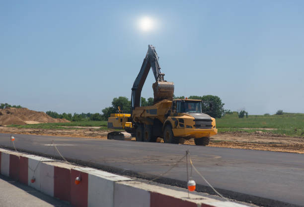 Excavator at Road Construction Site removing asphalt from pavement and preparing it for loading into the dump tuck. High angle view.