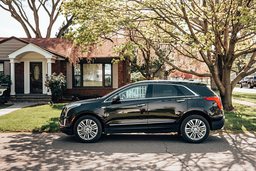 Lordship, CT, USA - May 4, 2019: A 2018 Cadillac XT5 at parked in an urban road of Lordship in  Connecticut . XT5 is the new suv by Cadillac, one of the most famous automotive brand in United States. Blossom tree in the background.