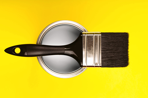 Demonstrating colors of year 2021 - Gray and Yellow. Brush with wooden handle on open can. Renovation concept.