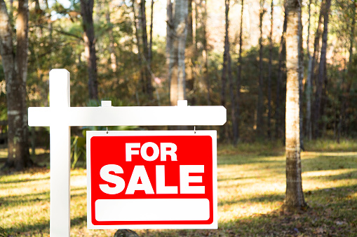 Home for sale with red and white real estate sign during the fall season.  Fall season with leaves on ground.  Front porch and windows in background.  Residential neighborhood.  Moving house, relocation concept.  Vacant Lot.