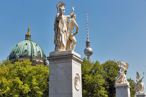 Berlin, Germany - July 14, 2018: Palace Bridge or Schlossbrucke sculpture closeup in Berlin Germany. Athena leads the young warrior into the fight. TV tower and Berliner Dom cathedral in the background.