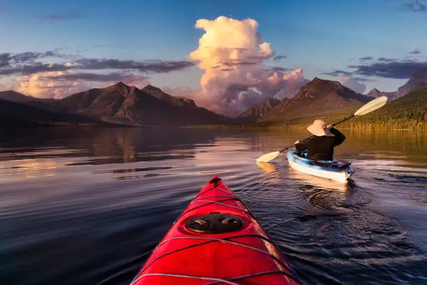 Adventurous Man Kayaking in Lake McDonald with American Rocky Mountains in the background. Colorful Sunset Sky. Taken in Glacier National Park, Montana, USA.