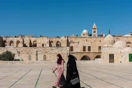 Two Muslim women wearing black hijab and walking at the square of the Golden Dome of the Rock, in an Islamic shrine located on the Temple Mount in the Old City, Jerusalem, Israel