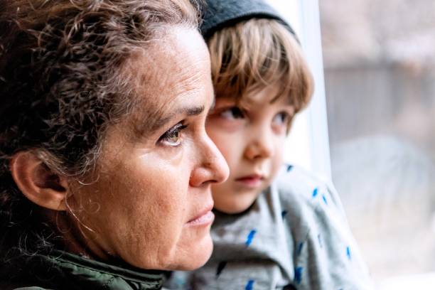 성숙한 여자 포즈 와 그녀의 아들, 매우 슬픈 때문에 covid-19 전염병 그녀의 직업의 손실에 대 한 걱정 창을 통해 찾고 - poverty 뉴스 사진 이미지