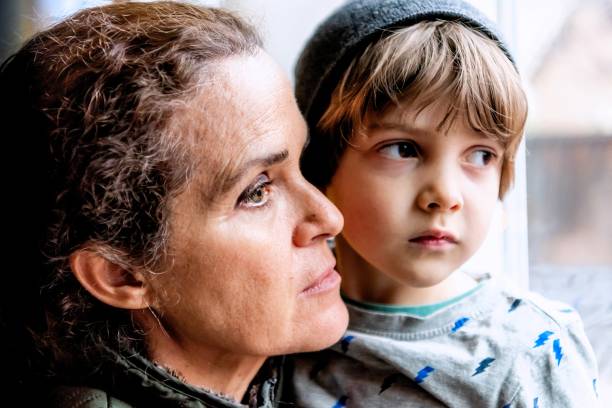 Mature woman posing with her son, very sad looking through window worried about loss of her job due Covid-19 pandemic Caucasian Mature woman posing with her son, very sad looking through window worried about loss of her job due Covid-19 pandemic family mother poverty sadness stock pictures, royalty-free photos & images