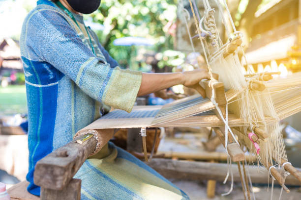 fille thaïlandaise tissant le textile thaï thaï traditionnel dans le jardin - weaving machine photos et images de collection