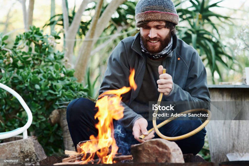 If you can't stand the heat you're not the grill-master Shot of a young man lighting a fire in preparation for a barbecue Barbecue Grill Stock Photo