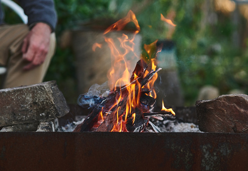 Shot of an unrecognisable man relaxing by an open fire at a barbecue outdoors