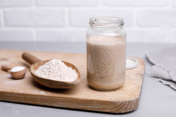 Sourdough Starter and Flour Active rye sourdough in glass jar and flour in wooden spoon. yeast starter stock pictures, royalty-free photos & images