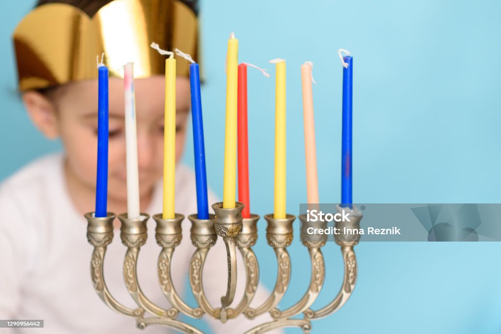 Little jewish boy puts candles on traditional menorah Kid celebrating Hanukkah Israel holiday. Little Jewish boy puts candles on traditional menorah with eight candles. Selective focus on yellow candle. Baby - Human Age Stock Photo