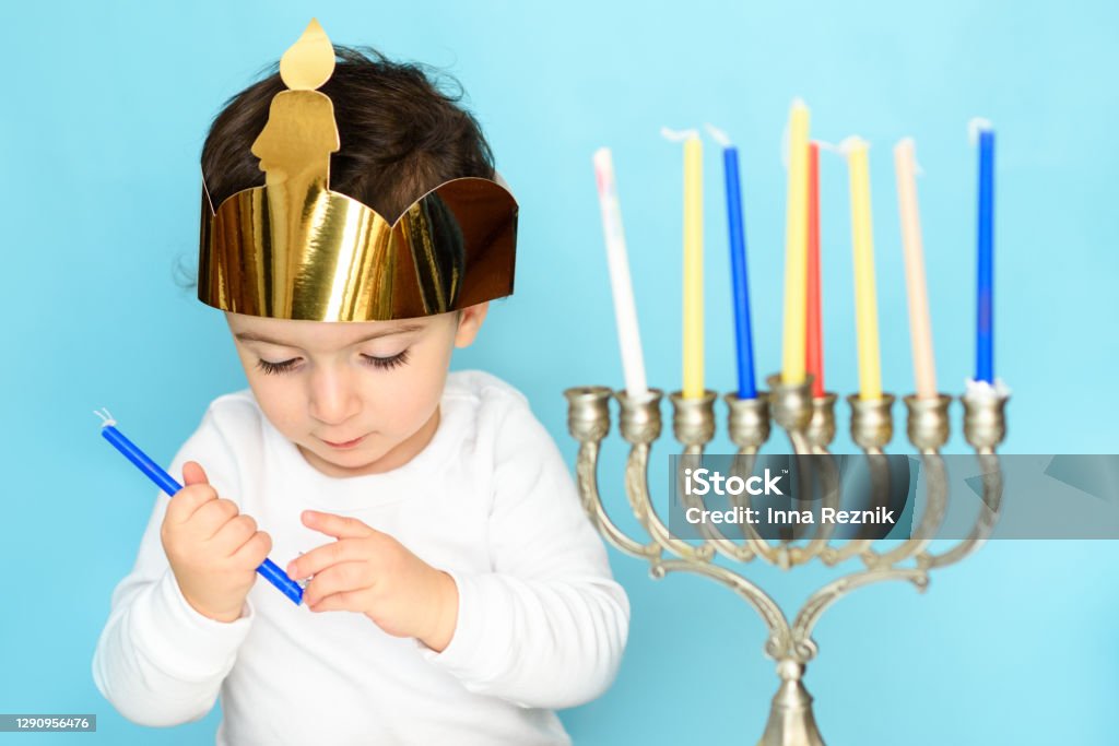 Little jewish boy puts candles on traditional menorah Kid celebrating Hanukkah Israel holiday. Little jewish boy puts candles on traditional menorah. Baby - Human Age Stock Photo