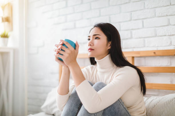 istock Depressed young woman sitting on bed at home 1290962165