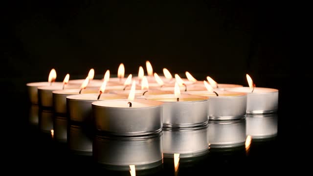 Close up of an arrangement of relaxing lit tea light candles and their reflection on a dark background. Relaxation and abstract concept.