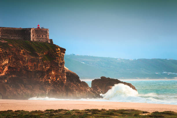Big waves on the coast of Atlantic ocean in Nazare, Portugal. Big waves on the coast of Atlantic ocean in Nazare, Portugal. View of the cape with lighthouse from the North beach nazare surf stock pictures, royalty-free photos & images