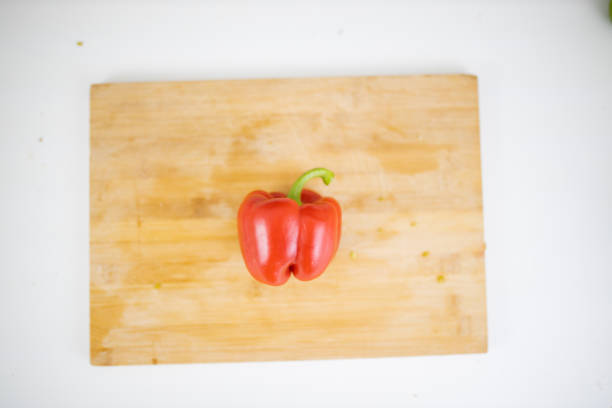 Whole red bell pepper on wooden cutting board. Above view of fresh vegetable on white table. Healthy meal preparation