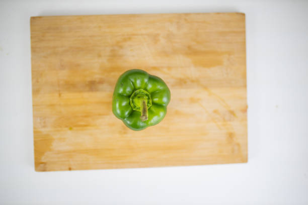 Whole green bell pepper on wooden cutting board. Above view of fresh vegetable on white table. Healthy meal preparation