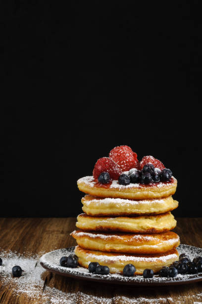 istock curd pancakes on a plate with blueberries and strawberries sprinkled with powdered sugar on a wooden surface and a dark background. side view. artistic moody vertical image with copy space 1290985407