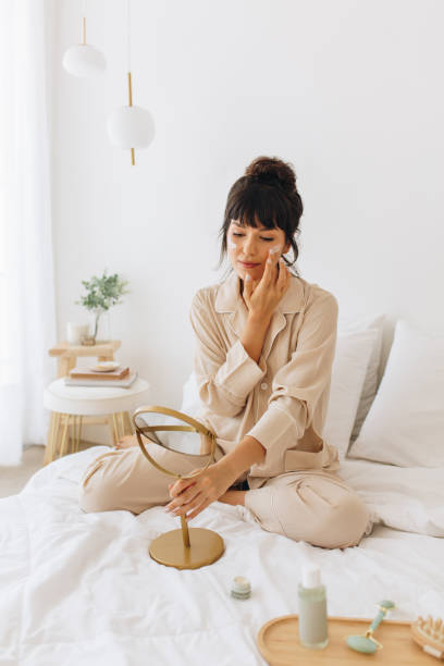 istock Young woman applying face cream sitting on bed 1290985754
