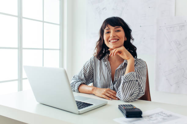istock Smiling female architect sitting at her office desk 1290985756