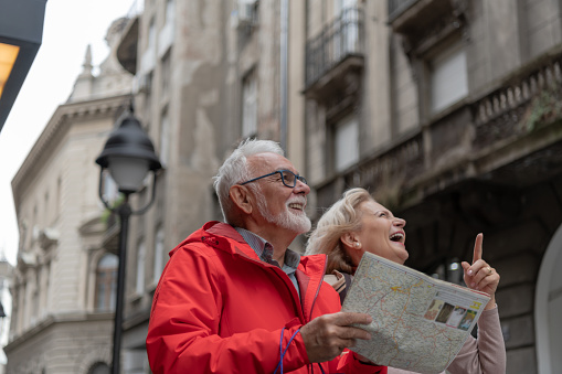 Married couple of tourists sightseeing city street with map - Happy husband and wife enjoying summer vacation together - Touristic life style concept with aged woman and man traveling European city