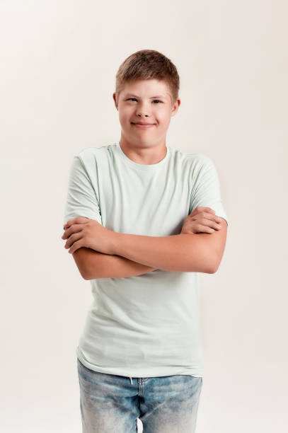 istock Teenaged disabled boy with Down syndrome smiling at camera while posing, standing with arms crossed isolated over white background 1290988047