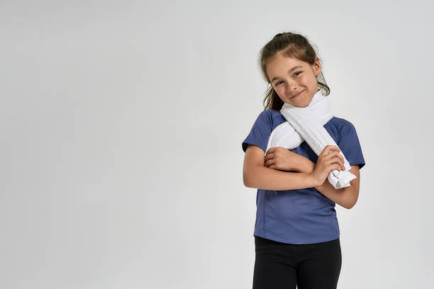 little sportive girl child in sportswear smiling at camera, holding towel around her neck while standing isolated over white background - gymnastics smiling little girls only isolated on white imagens e fotografias de stock