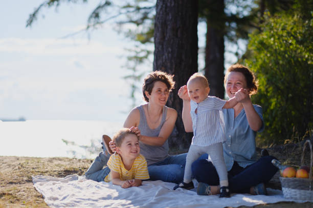 familia lesbiana homosexual con dos hijos, un hijo y una hija. dos madres y niños en un picnic al aire libre. bosque y mar. - baby mother summer park fotografías e imágenes de stock